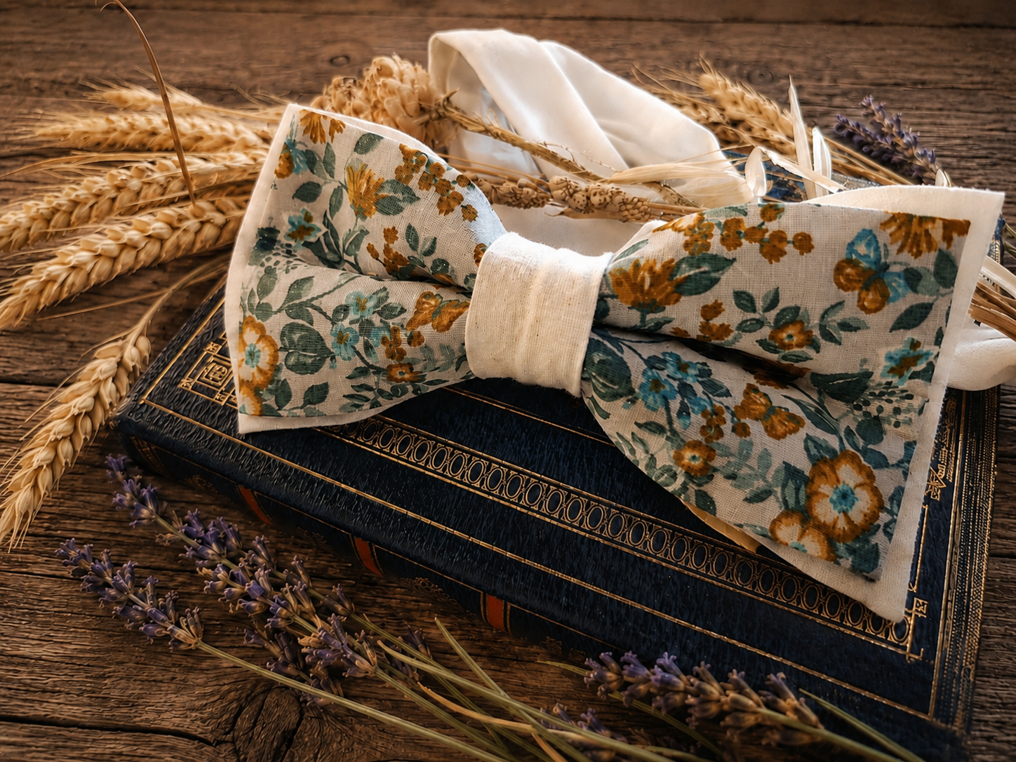 Nœud papillon Liberty Marcel Fleur Bleue posé sur un livre ancien, entouré de lavande et d'épis de blé dans une ambiance champêtre provençale.