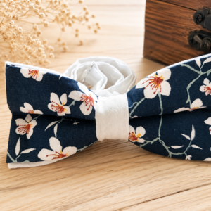 Nœud papillon Marcel Sakura en coton bleu marine à fleurs de cerisier, présenté sur une table en bois clair.