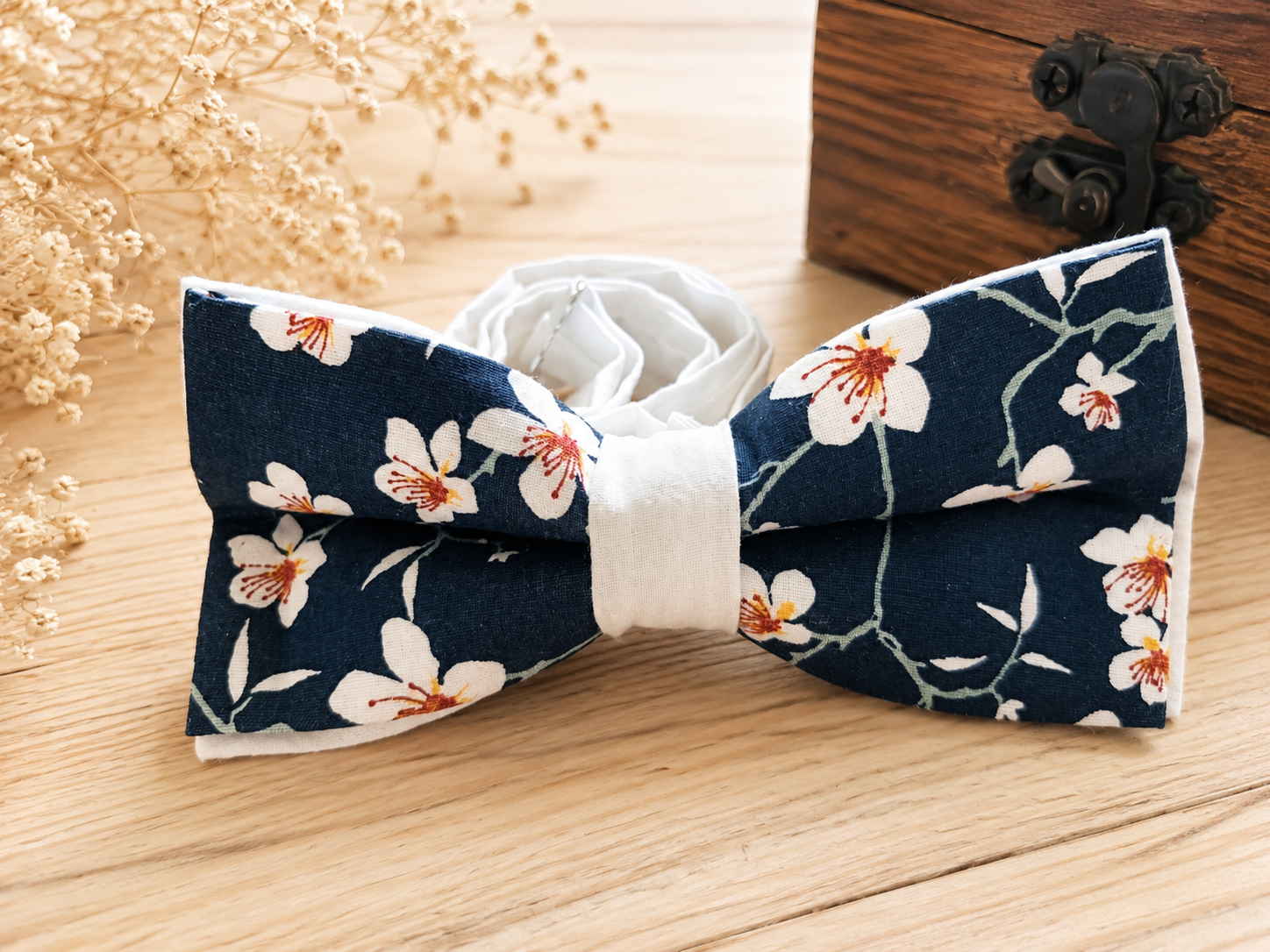 Nœud papillon Marcel Sakura en coton bleu marine à fleurs de cerisier, présenté sur une table en bois clair.